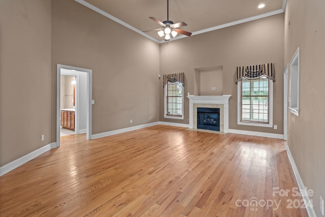 unfurnished living room with light wood-type flooring, ornamental molding, a high ceiling, and a tiled fireplace