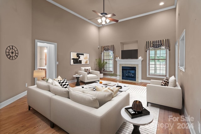 living room with a tiled fireplace, a towering ceiling, ornamental molding, and light hardwood / wood-style flooring