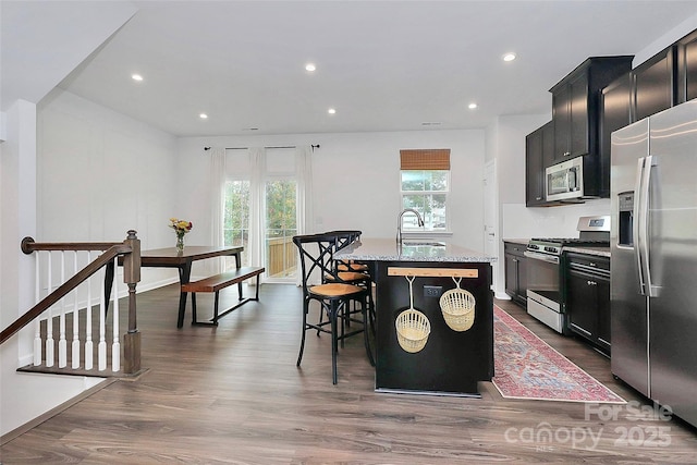 kitchen with a kitchen bar, sink, appliances with stainless steel finishes, light stone countertops, and a kitchen island with sink