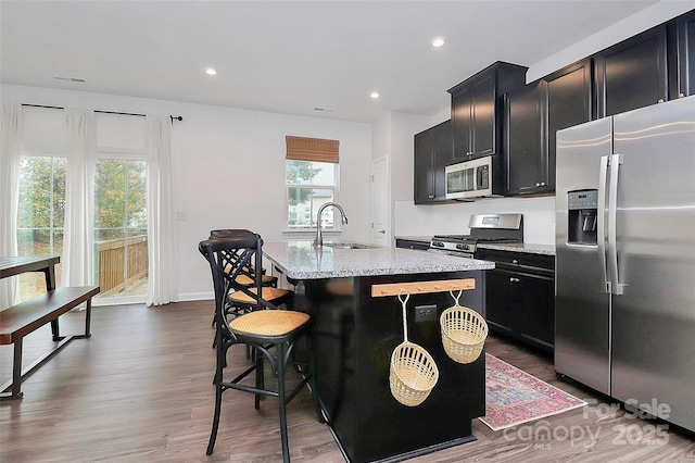 kitchen featuring appliances with stainless steel finishes, a breakfast bar, sink, light stone counters, and a center island with sink