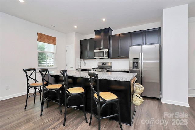 kitchen featuring light stone countertops, appliances with stainless steel finishes, a center island with sink, and a kitchen breakfast bar