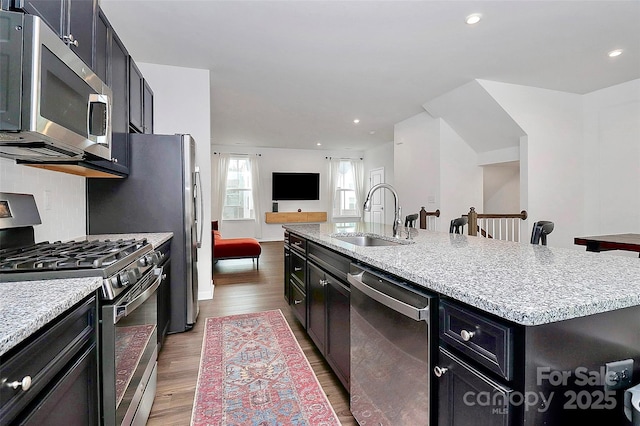 kitchen featuring sink, a center island with sink, appliances with stainless steel finishes, light hardwood / wood-style floors, and decorative backsplash