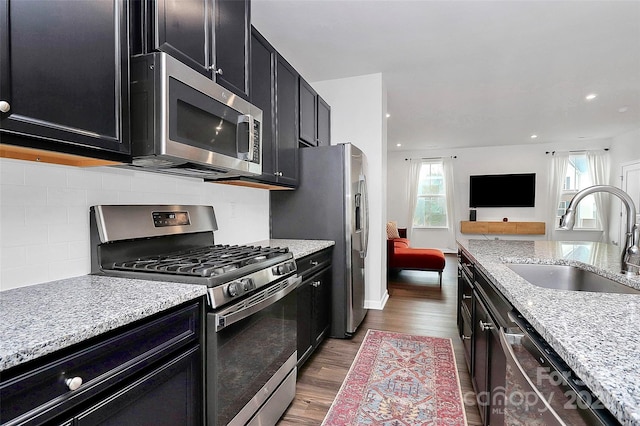 kitchen with sink, stainless steel appliances, light stone counters, wood-type flooring, and decorative backsplash