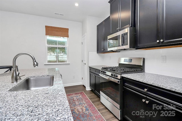 kitchen with dark wood-type flooring, sink, light stone counters, tasteful backsplash, and appliances with stainless steel finishes