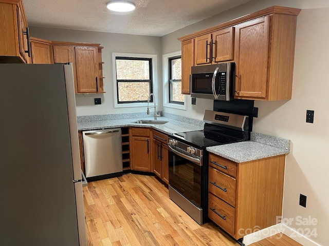 kitchen with sink, light stone counters, appliances with stainless steel finishes, a textured ceiling, and light hardwood / wood-style flooring