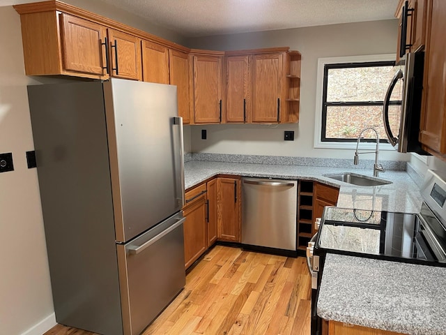 kitchen with light stone countertops, appliances with stainless steel finishes, sink, and light hardwood / wood-style floors