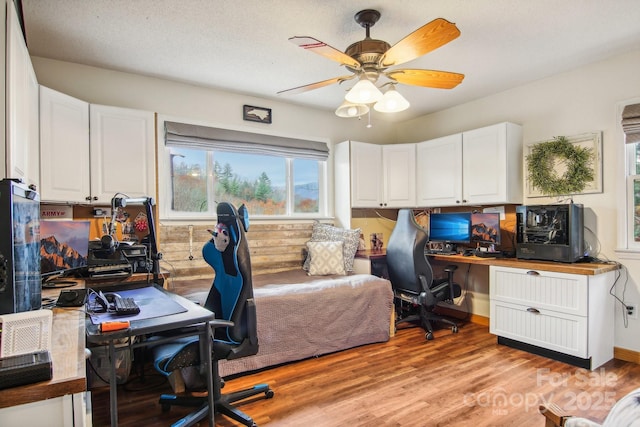 home office with ceiling fan, built in desk, and light hardwood / wood-style flooring