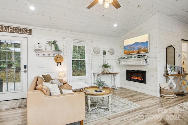 living room featuring vaulted ceiling, wood walls, ceiling fan, wooden ceiling, and light wood-type flooring