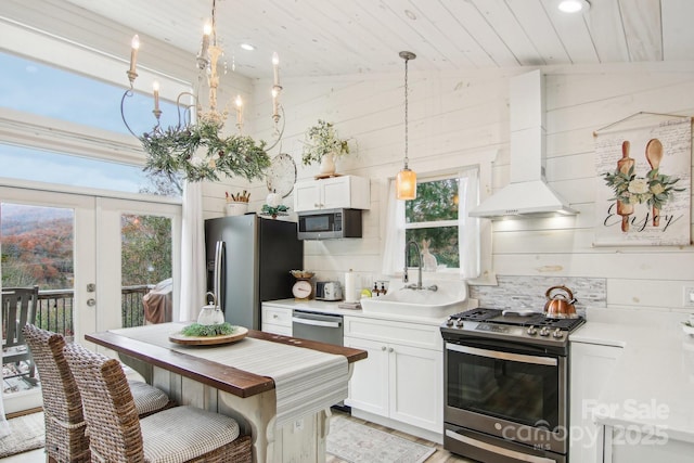 kitchen with appliances with stainless steel finishes, pendant lighting, sink, white cabinets, and wall chimney range hood