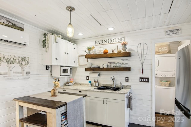 kitchen with stacked washer and dryer, sink, hanging light fixtures, and white cabinets