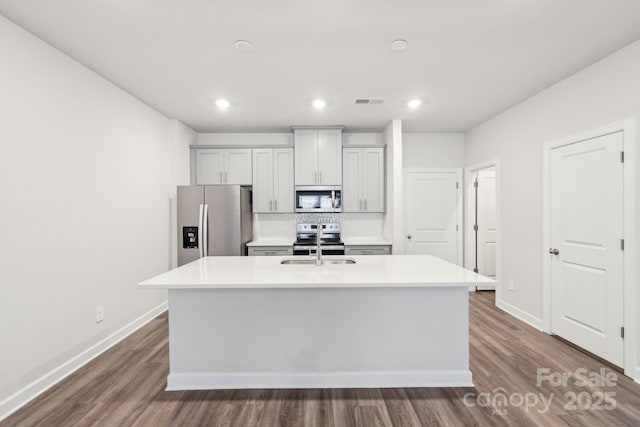 kitchen with tasteful backsplash, an island with sink, appliances with stainless steel finishes, and dark wood-type flooring