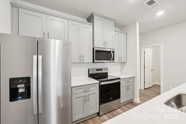 kitchen featuring gray cabinetry, sink, light hardwood / wood-style flooring, and appliances with stainless steel finishes