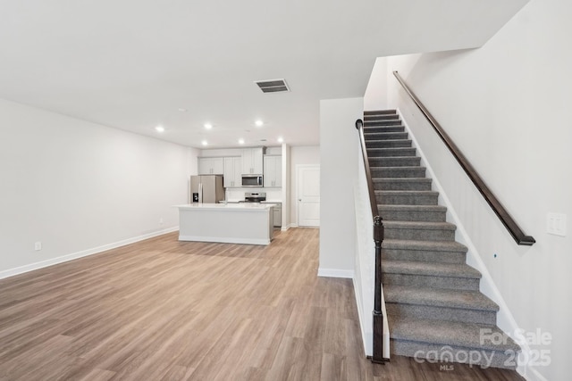 unfurnished living room featuring recessed lighting, stairway, visible vents, light wood finished floors, and baseboards