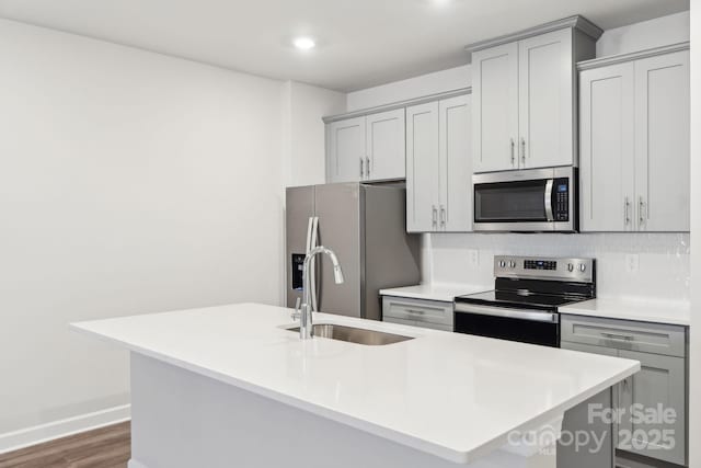 kitchen with gray cabinets, an island with sink, appliances with stainless steel finishes, and backsplash