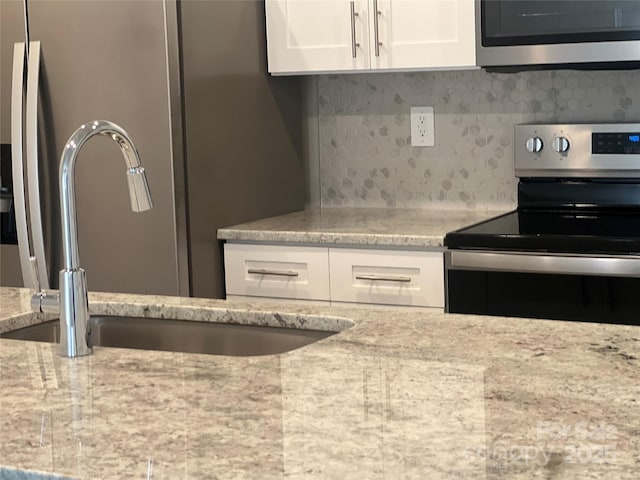 kitchen featuring stainless steel appliances, light stone counters, decorative backsplash, sink, and white cabinetry