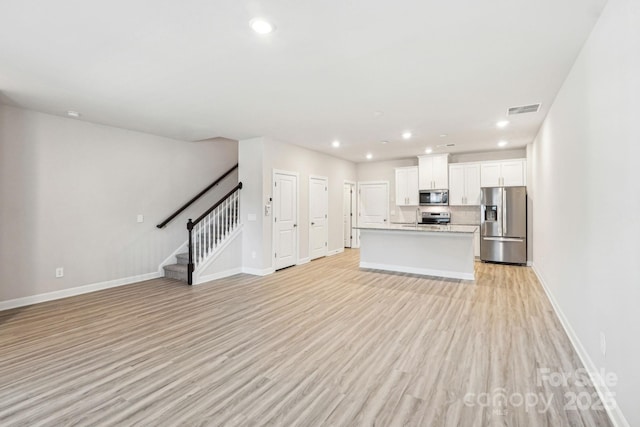 kitchen with appliances with stainless steel finishes, white cabinets, backsplash, a center island with sink, and light wood-type flooring