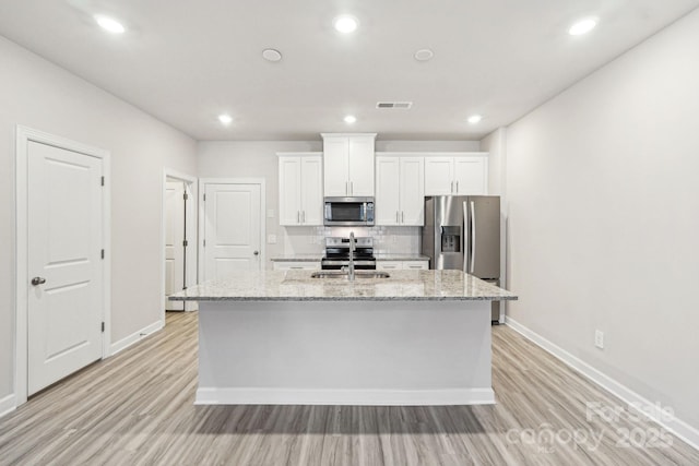 kitchen featuring sink, white cabinetry, stainless steel appliances, light stone counters, and an island with sink