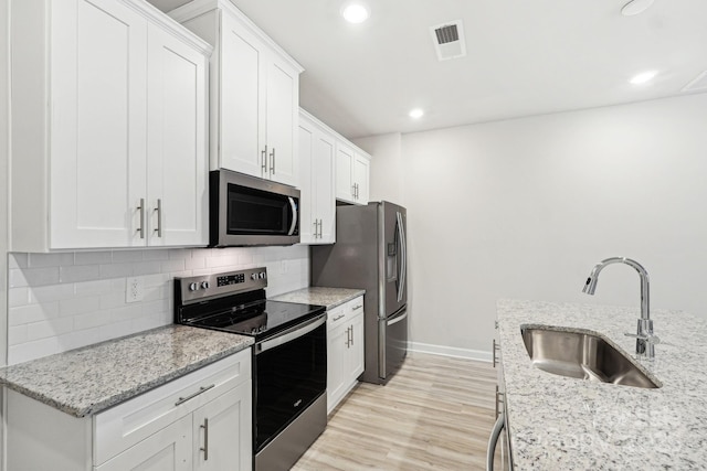 kitchen with stainless steel appliances, white cabinetry, light stone countertops, and sink