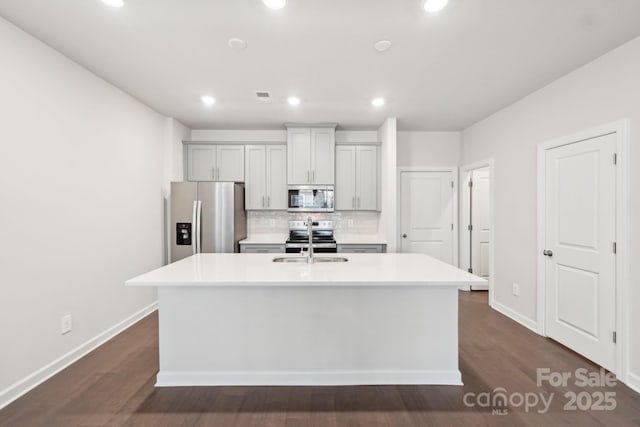 kitchen featuring sink, decorative backsplash, stainless steel appliances, and a center island with sink