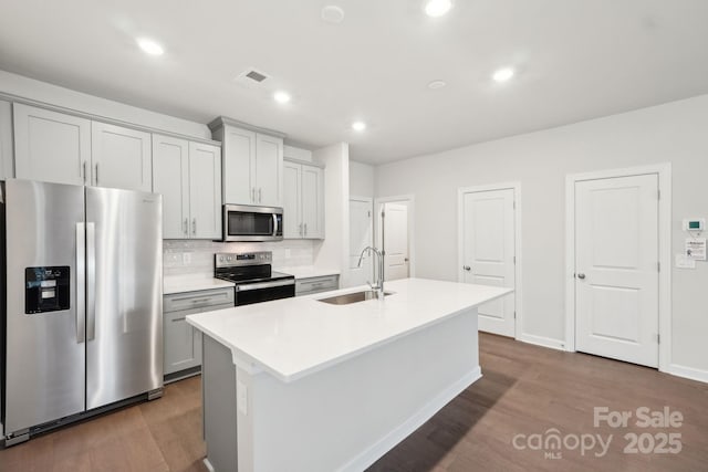 kitchen with sink, appliances with stainless steel finishes, dark hardwood / wood-style floors, a kitchen island with sink, and backsplash