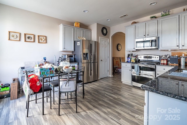 kitchen featuring appliances with stainless steel finishes, dark stone counters, and hardwood / wood-style floors