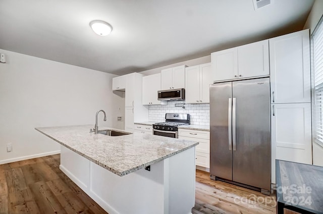 kitchen featuring stainless steel appliances, white cabinets, sink, and an island with sink