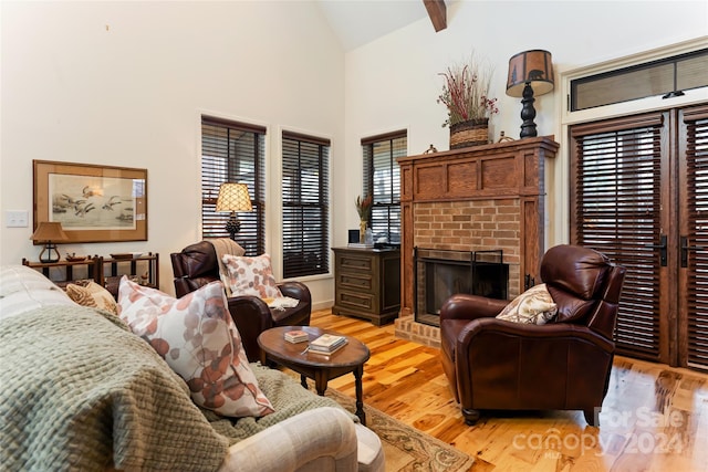 living area featuring a fireplace, high vaulted ceiling, light hardwood / wood-style floors, and beamed ceiling