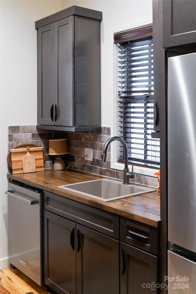 kitchen featuring butcher block counters, sink, stainless steel appliances, backsplash, and light wood-type flooring