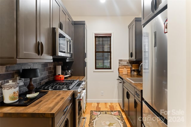 kitchen featuring appliances with stainless steel finishes, light wood-type flooring, butcher block countertops, and tasteful backsplash