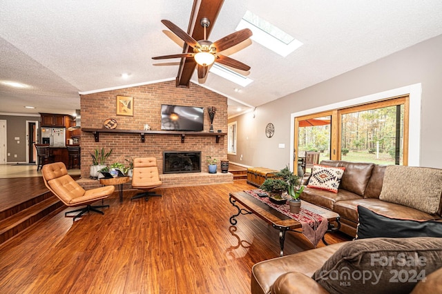 living room featuring hardwood / wood-style flooring, lofted ceiling with skylight, ceiling fan, a textured ceiling, and a brick fireplace