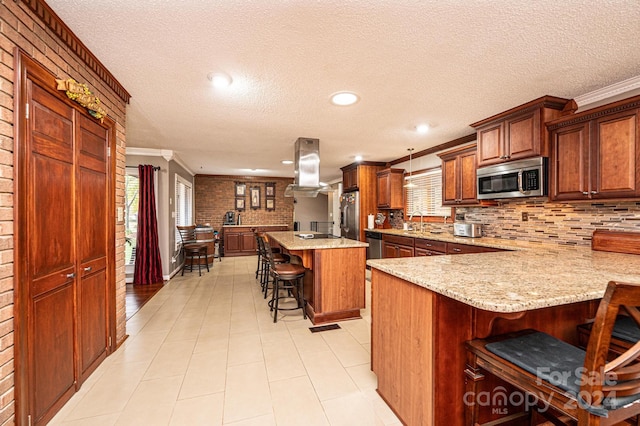 kitchen with a center island, ornamental molding, island exhaust hood, a breakfast bar, and appliances with stainless steel finishes