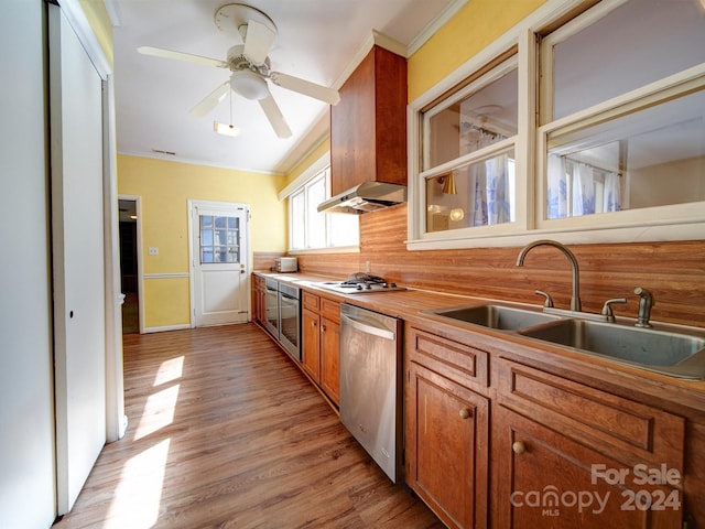 kitchen featuring sink, stainless steel appliances, wall chimney range hood, light wood-type flooring, and ornamental molding