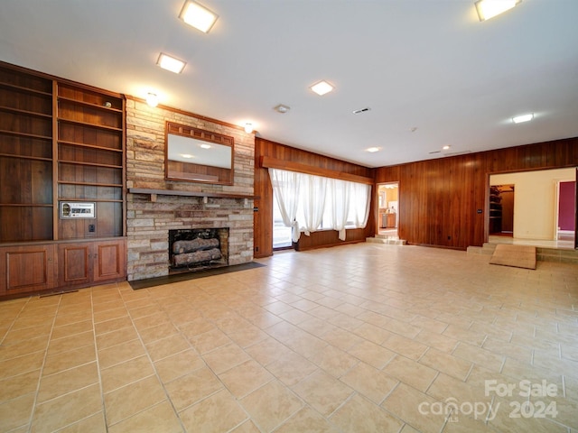 unfurnished living room with built in shelves, wooden walls, a fireplace, and light tile patterned flooring