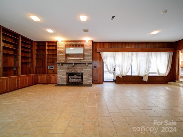 unfurnished living room featuring built in shelves, wood walls, and a stone fireplace