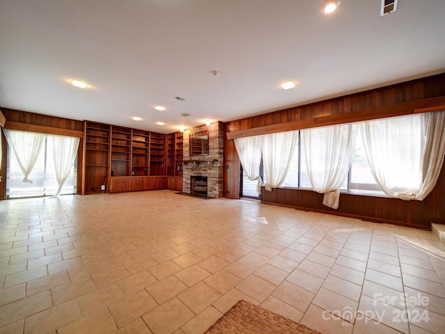 unfurnished living room featuring a fireplace, wooden walls, and built in features