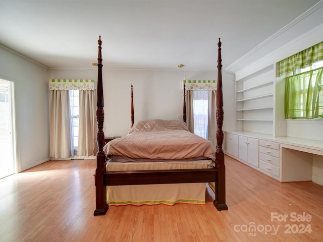 bedroom with crown molding, built in desk, and light wood-type flooring