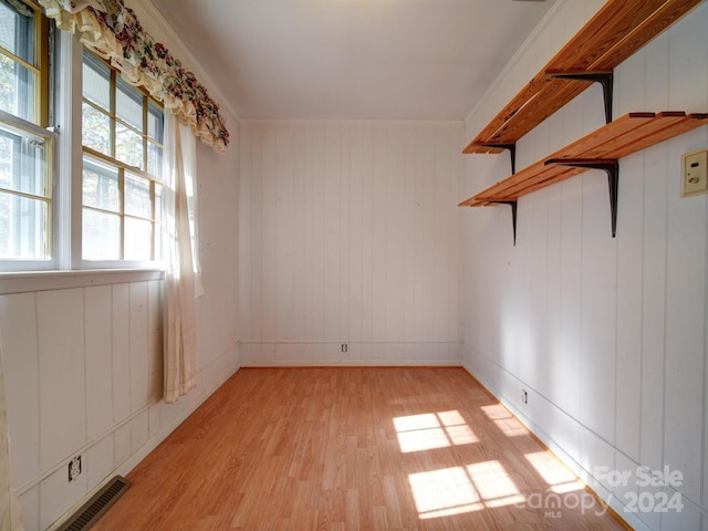 unfurnished room featuring light wood-type flooring, crown molding, and wood walls