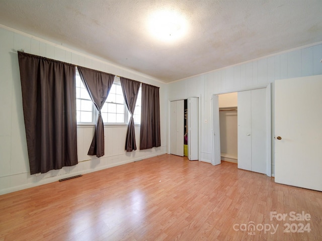 unfurnished bedroom with two closets, a textured ceiling, and light hardwood / wood-style flooring