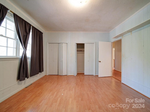 unfurnished bedroom with two closets, crown molding, a textured ceiling, and light hardwood / wood-style flooring