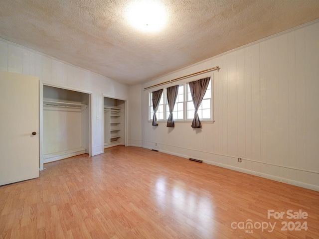 unfurnished bedroom featuring wood walls, light hardwood / wood-style floors, a textured ceiling, and multiple closets