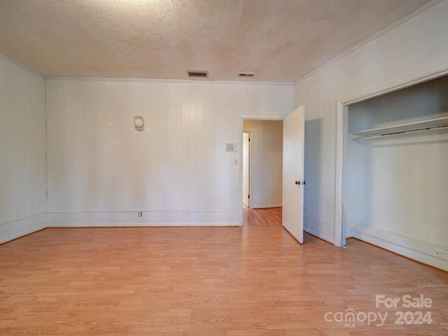 unfurnished bedroom with a closet, light hardwood / wood-style flooring, crown molding, and a textured ceiling