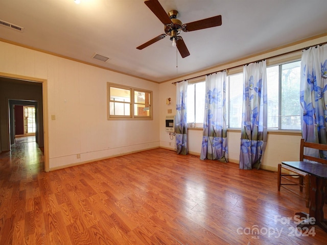 interior space featuring heating unit, ceiling fan, wood-type flooring, and ornamental molding