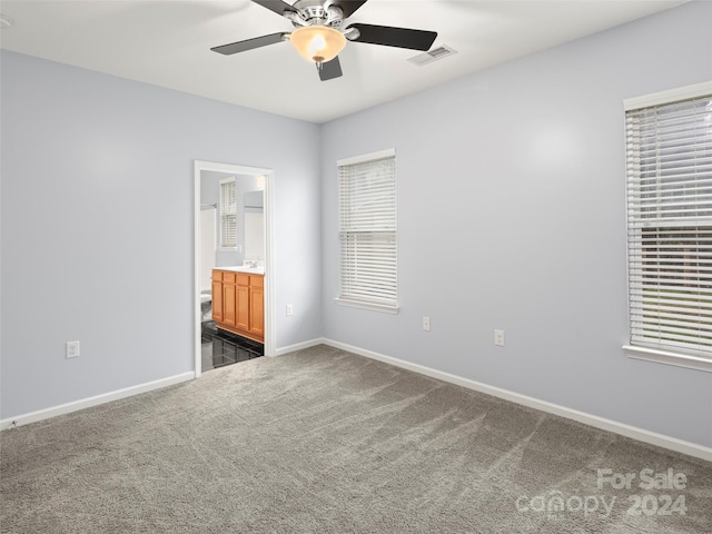 unfurnished bedroom featuring ensuite bathroom, dark colored carpet, and ceiling fan