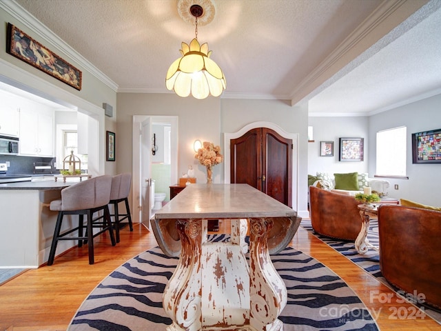 dining area featuring a healthy amount of sunlight, light hardwood / wood-style flooring, a textured ceiling, and ornamental molding