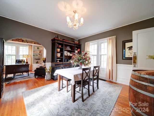 dining space featuring built in features, a chandelier, wood-type flooring, and ornamental molding