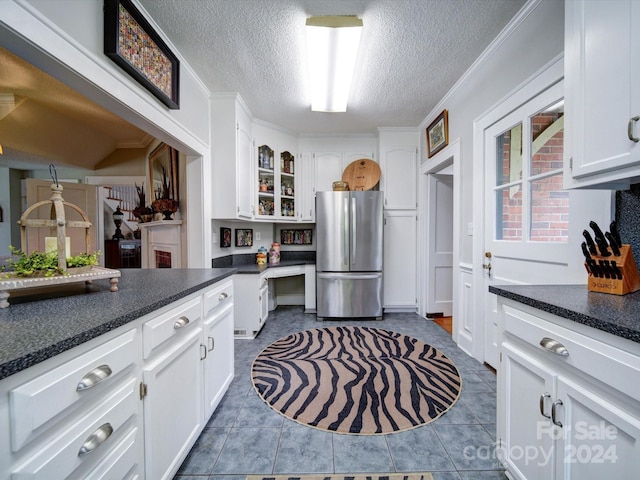 kitchen featuring ornamental molding, stainless steel fridge, white cabinetry, a textured ceiling, and dark tile patterned flooring