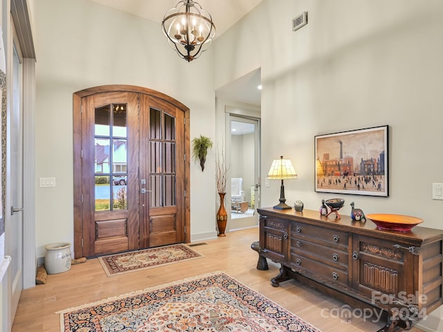 entryway with a high ceiling, light wood-type flooring, french doors, and a notable chandelier