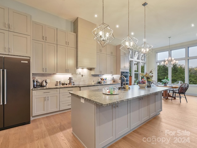 kitchen with high end refrigerator, hanging light fixtures, light hardwood / wood-style floors, and a kitchen island with sink