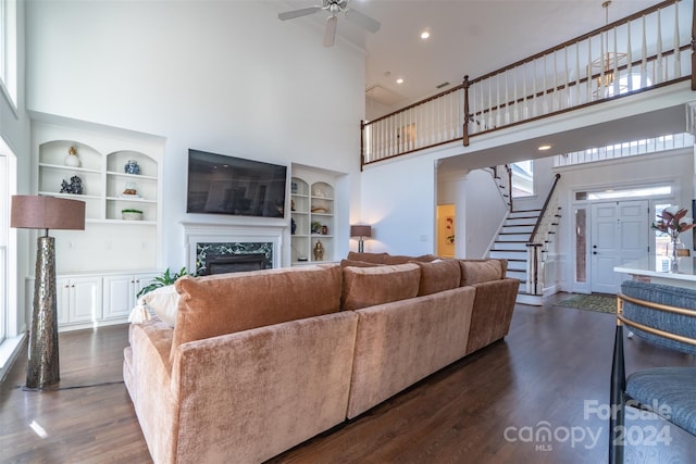 living room featuring a premium fireplace, dark hardwood / wood-style flooring, a towering ceiling, and built in features