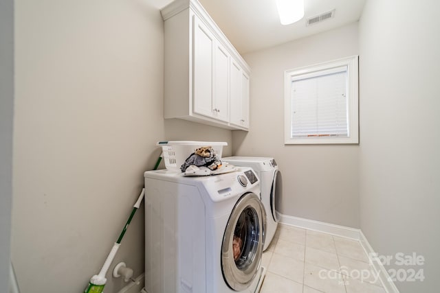 clothes washing area with washer and dryer, cabinets, and light tile patterned flooring